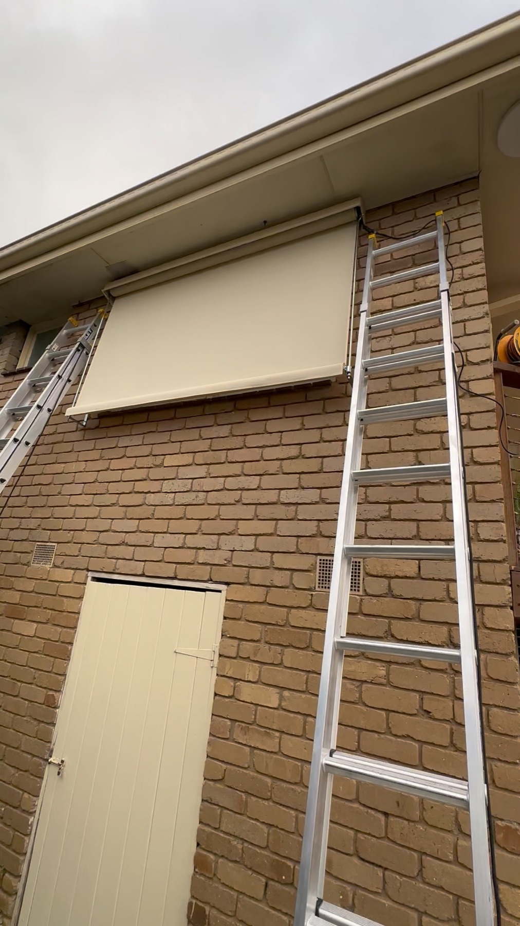 Cream auto awning installed high on a brick wall