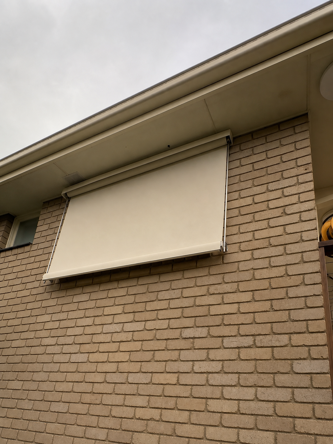 Cream fixed guide awning fitted on a brick wall