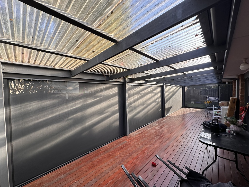 Multiple dark mesh Ziptrak blinds along a long covered deck